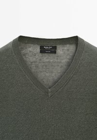 Maglione a V in 100% lino di colore verde oliva spento. Presenta un collo a costine e una finitura morbida e testurizzata.
