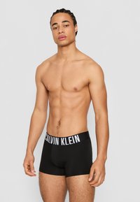 Schwarze Baumwoll-Boxershorts mit einem weißen Calvin Klein-Logo am Bund. Die Passform ist eng, und der Stoff hat eine glatte Textur.