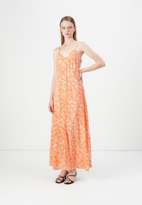Maxi-mekko elävän oranssin värissä valkoisella aalto-kuviolla, jossa on ohuet olkaimet ja sulava siluetti, valmistettu kevyestä kankaasta.