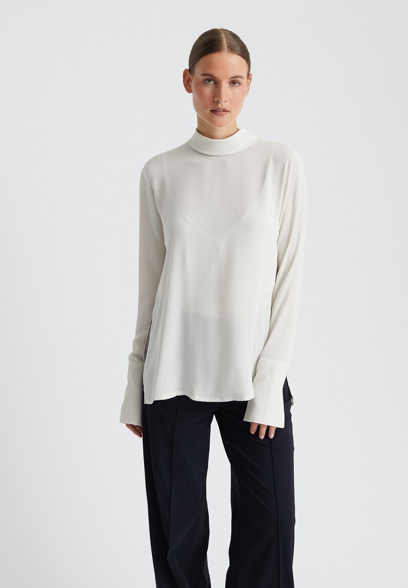 Witte langemouwenblouse met een hoge kraag, van lichtgewicht, gladde stof, met een ontspannen pasvorm en gespleten manchetten, gecombineerd met zwarte broek.