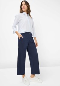 Light blue striped shirt with a collar, navy wide-leg trousers, and white sneakers. The outfit features a casual fit and crisp lines.