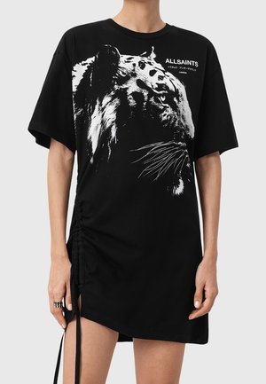 Personne portant une robe T-shirt noire oversize avec un imprimé visage de tigre blanc et un petit texte ALLSAINTS sur la poitrine.