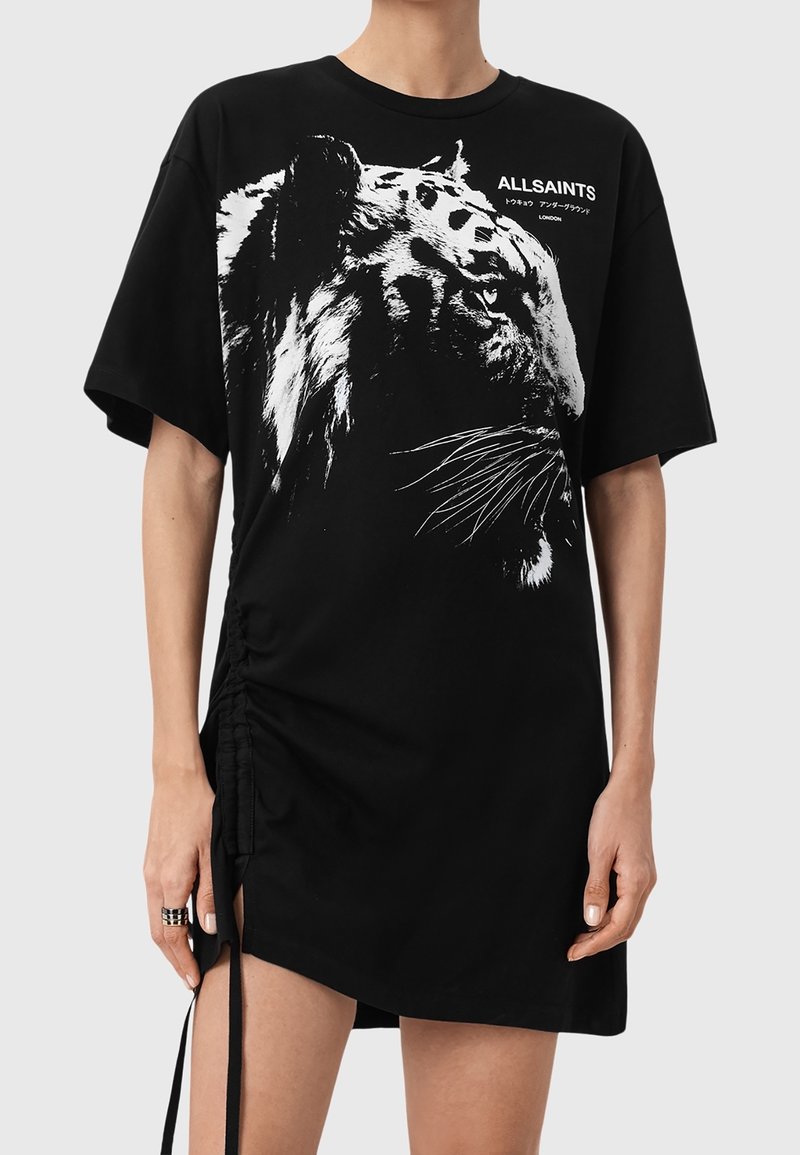 Personne portant une robe T-shirt noire oversize avec un imprimé visage de tigre blanc et un petit texte ALLSAINTS sur la poitrine.