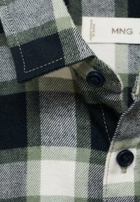 Camicia a quadri verde e blu navy con colletto, caratterizzata da bottoni scuri, cuciture dettagliate e tessuto di cotone testurizzato.