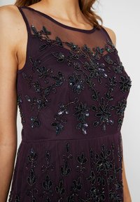 Sleeveless dark purple dress with sheer neckline and intricate floral bead and sequin embellishments on bodice and skirt.