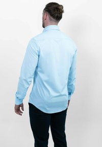 Lichtblauw overhemd met lange mouwen en kraag, met een gladde textuur en een gebogen zoom, gecombineerd met donkere broek. Gezien vanaf de achterkant.