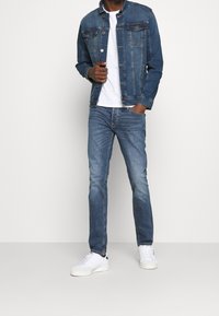 Farkkutakki klassisella designilla, sininen pesu, napit yksityiskohtina, yhdistetty vaaleansinisiin farkkuihin ja valkoisiin lenkkareihin. Yksinkertainen valkoinen t-paita alla.