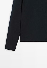 Sort striktop med lange ærmer og lige snit, der har en blød tekstur og minimalistisk design, med fokus på enkelhed og komfort.