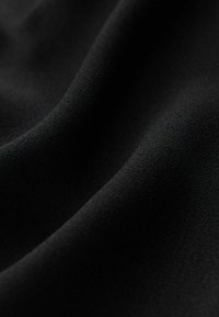 Tissu noir avec une texture lisse et mate, présentant des plis doux et des dégradés. Des détails fins en gros plan mettent en évidence sa surface uniforme.