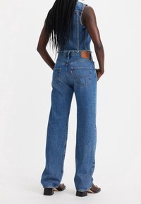 Mono de mezclilla con un diseño ajustado y sin mangas, bordes deshilachados y una silueta de pierna ancha. Color azul claro con costura típica y bolsillos.