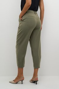 Pantalons verts raccourcis avec poches latérales, texture lisse, coupe ajustée et détails subtils sur les poches arrière, associés à des talons beiges.
