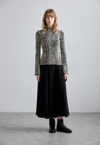 Černo-bílý pruhovaný pletený top s vysokým výstřihem, v kombinaci s černou skládací dlouhou sukní a černými kotníkovými botami. Hladké textury po celém outfitu.