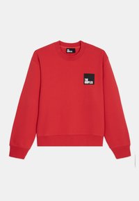 Sudadera roja de algodón, con un cuello redondo, puños acanalados y un pequeño parche negro de logo en el pecho. Diseño simple y casual.