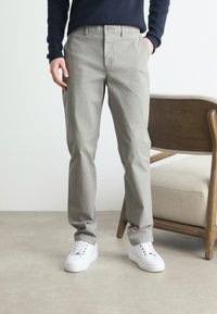 Light gray cotton trousers with a straight cut, featuring a front button closure, side pockets, and worn with white sneakers.