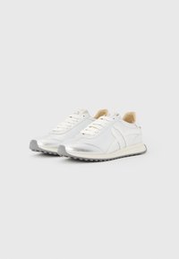 Λευκά αθλητικά παπούτσια με μεταλλικές ασημί λεπτομέρειες, με λείο υφή, στρογγυλή μύτη και επίπεδη ελαστική σόλα. Σχέδιο με κορδόνια και διακριτικό λογότυπο.