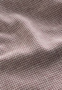 Gros plan sur un tissu texturé rose et marron avec un petit motif à carreaux et des plis doux créant des ombres.