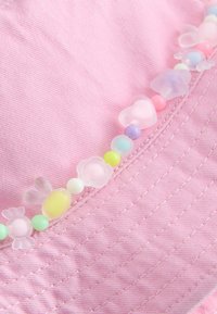 Nahaufnahme eines rosa Stoffes mit einer genähten Naht, verziert mit einer Perlenkette aus pastellfarbenen Perlen in Blumen-, Herz- und runden Formen.