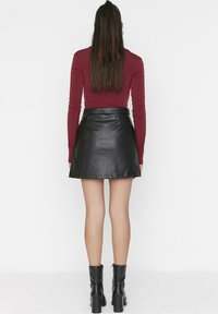 Jupe en cuir noir avec un design évasé, taille haute et fermeture éclair au dos. Associée à un haut ajusté bordeaux à manches longues et des bottines noires.