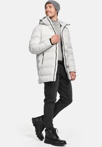 Puffjakke i lys grå med en aftagelig hætte, lynlåslukning og sorte detaljer. Kombineret med sorte slim-fit bukser og støvler.