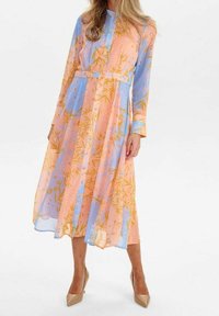 Robe fluide longueur cheville en rose pastel et bleu avec un motif floral. Manches longues, boutonnée devant, et taille cintrée soulignent la silhouette.