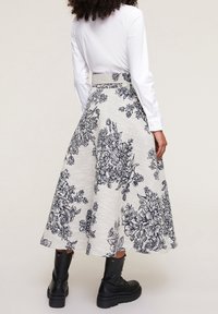Floral-patterned midi skirt in beige and navy, featuring a structured waistband and A-line shape. Worn with black lace-up boots.