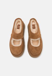 Brown suede shoes with a fuzzy interior, featuring a Velcro strap over the open top and a textured rubber sole.