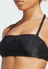 Čierny rebrovaný bikini top s tenkými nastaviteľnými ramienkami, ktorý má na prednej strane jemné logo a hladkú textúru.