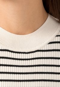 Weißer gerippter Pullover mit schwarzen horizontalen Streifen; verfügt über einen runden Ausschnitt und eine glatte Textur.
