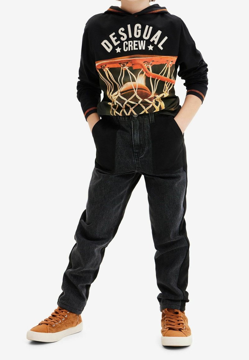 Czarna bluza z kapturem z grafiką koszykarską i napisem "DESIGUAL CREW", zestawiona z czarnymi i ciemnoniebieskimi dżinsami oraz brązowymi trampkami.