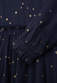 Marineblaues Kleid mit goldenem Sternenmuster, gerippter Textur, elastischen Bündchen und gerafftem Taillenbereich. Verfügt über subtile schimmernde Details im gesamten Kleid.