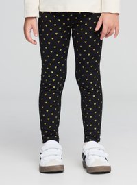 Leggings nere con un motivo di piccoli cuori dorati, materiale elasticizzato, forma aderente, abbinati a sneakers bianche e grigie.