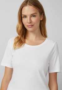 Witte T-shirt met korte mouwen en een ronde hals. Gemaakt van soepele, lichte stof, met een aansluitende pasvorm en minimale naaddetails.