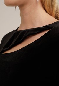 Crni baršunasti top s drapiranim dekolteom i izrezom. Glatka tekstura i kroj koji naglašava elegantnost dizajna.