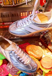 Des baskets argentées et blanches suspendues parmi des jetons et pièces colorés du casino de Las Vegas à l'intérieur d’un jeu d’arcade à pince.
