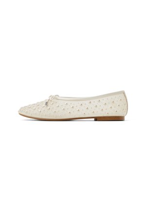 Chaussure plate de couleur crème, faite d'un matériau lisse, ornée d'accents en relief ressemblant à des perles, avec un bout arrondi et un design minimaliste.