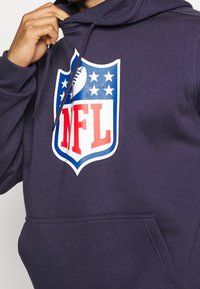 Námořnická mikina s kapucí s velkým logem NFL v červené a modré barvě, s bílými akcenty a hvězdami, vyrobená z měkké látky s přední kapsou.