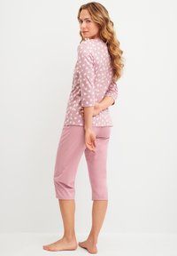 Hellrosa Pyjama-Set mit einem Oberteil, das kleine weiße Herzmuster und Drei-Viertel-Ärmel hat, kombiniert mit schlichten hellrosa cropped Hosen.