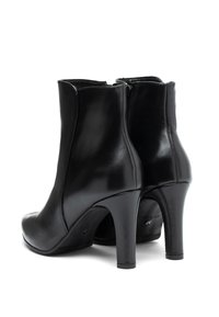 Botines de piel negra hasta el tobillo con una textura suave, punta redonda y altos tacones de aguja. Presentan un diseño elegante y cierre de cremallera en la parte trasera.