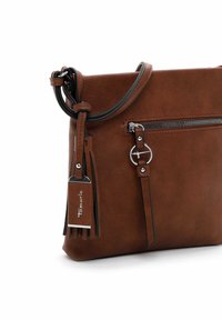 Hnědá crossbody taška z umělé kůže s texturovaným povrchem, zipovou kapsou a dekorativním třásním se metalickým štítkem.