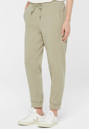 Beige Jogginghosen mit schmal zulaufenden Beinen, Kordelzug an der Taille und hochgekrempelten Säumen, getragen mit weißen Schnürsenkelsneakern.
