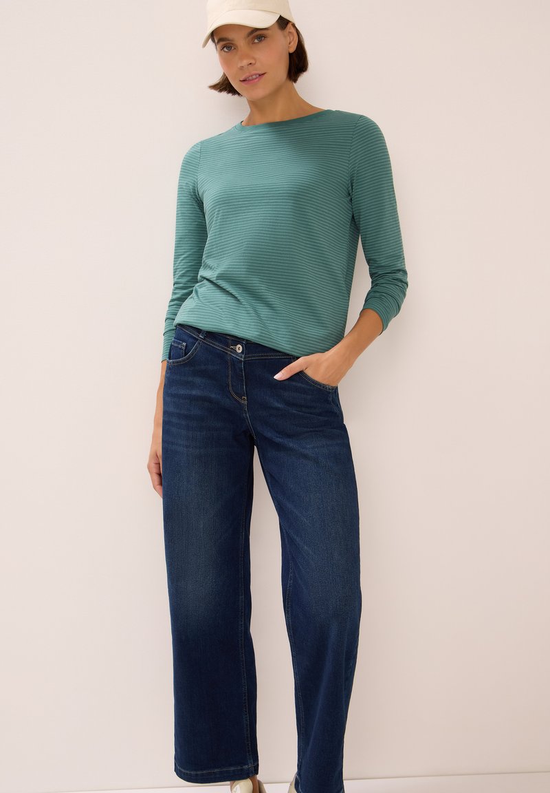 Long-sleeve, teal striped top paired with wide-leg, dark denim jeans. A cream cap completes the outfit. Simple, casual styling.