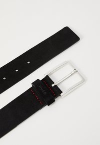 Zwarte suède riem met een zilveren rechthoekige gesp en rode stikdetails. Bevat vijf gaatjes voor maataanpassing en heeft schone randen.