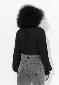 Blouse noire à manches longues avec un col froncé, assortie à un jean gris déchiré taille haute avec poches arrière et taille élastique.