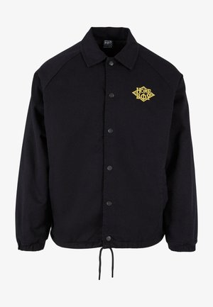 Sort jakke med knaplukning fortil, raglanærmer og et broderet gult logo med teksten "HOME BOY" på venstre bryst. Inkluderer justerbar snor.