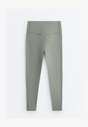 Magas derekú, tompa zöld, teljes hosszúságú leggings oldalsávos díszítéssel, sima, rugalmas anyagból, fehér háttéren lapra helyezve.
