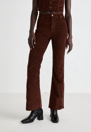 Person wearing high-waisted brown corduroy pants with front button and zipper, paired with cropped brown vest and black heeled ankle boots.