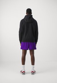 Hanorac negru cu glugă, pantaloni scurți din plasă violet, șosete albe și adidași negri cu roșu. Se potrivește strâns, cu o textură netedă și un design casual.