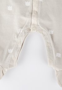 Romper per bebè color beige chiaro con bottoni a pressione lungo la cucitura interna e piccolo motivo di corone bianche su tessuto morbido.