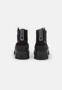 Bottes noires jusqu'à la cheville avec une finition texturée, dotées d'une semelle en caoutchouc épaisse, de deux poignées et d'une marque blanche le long de l'arrière pour un détail supplémentaire.