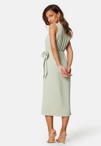 Světle zelené, bezrukávové midi šaty s nařaseným pasem a mašlí na zadní straně. Hladký, splývavý materiál s uvolněným střihem.